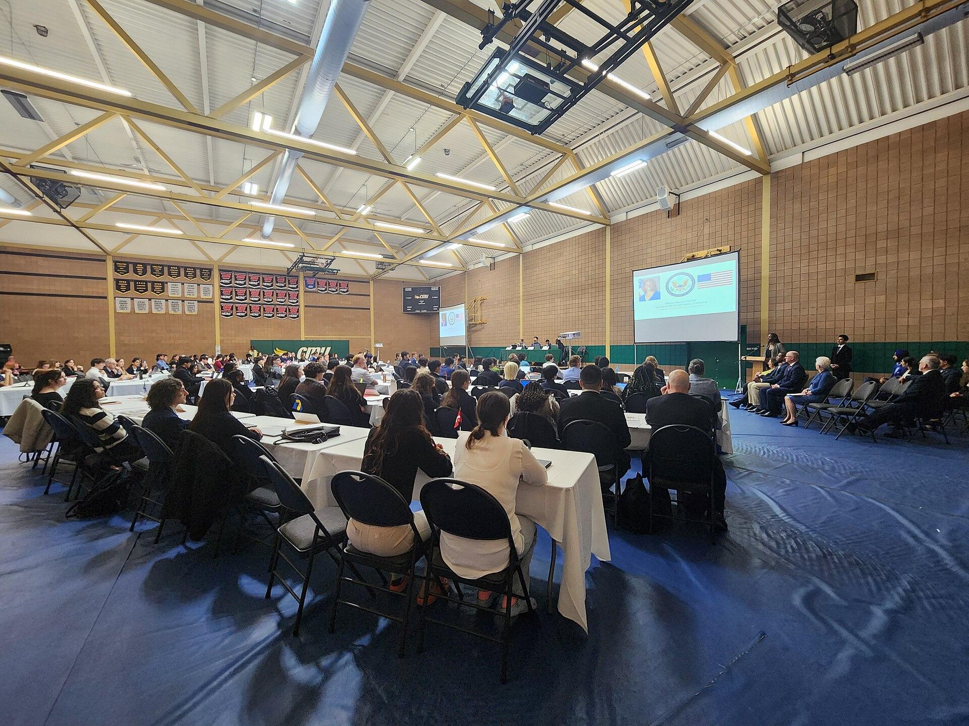 Students in business attire seated at draped tables during a Model United Nations assembly